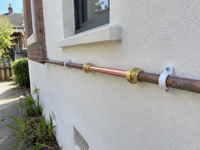 Repaired copper water pipe fixed to an exterior rendered wall below a window in Dulwich Hill